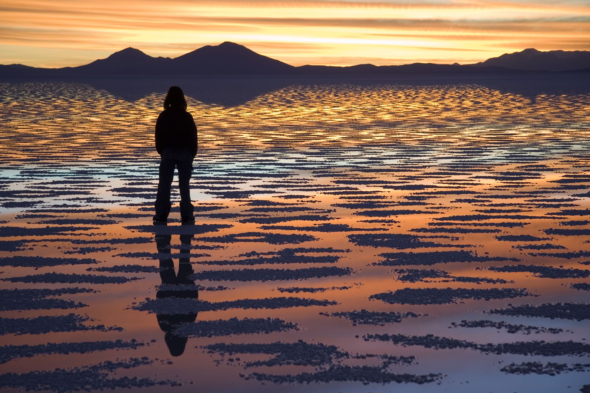 A lone figure silhouetted at sunset on the reflective Salar de Uyuni